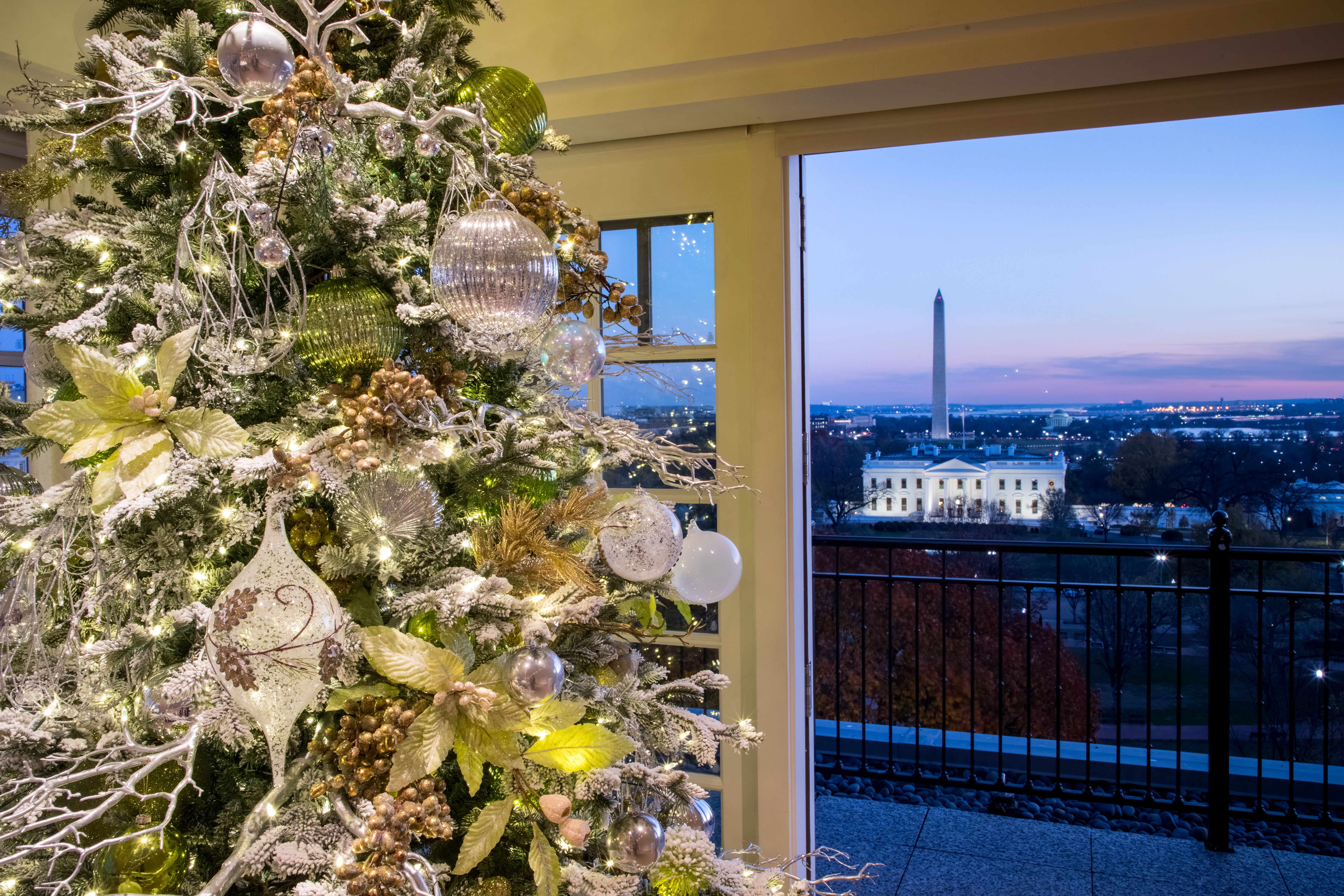 A decorated Christmas tree stands in front of a window showing the Washington Monument and cityscape at dusk.