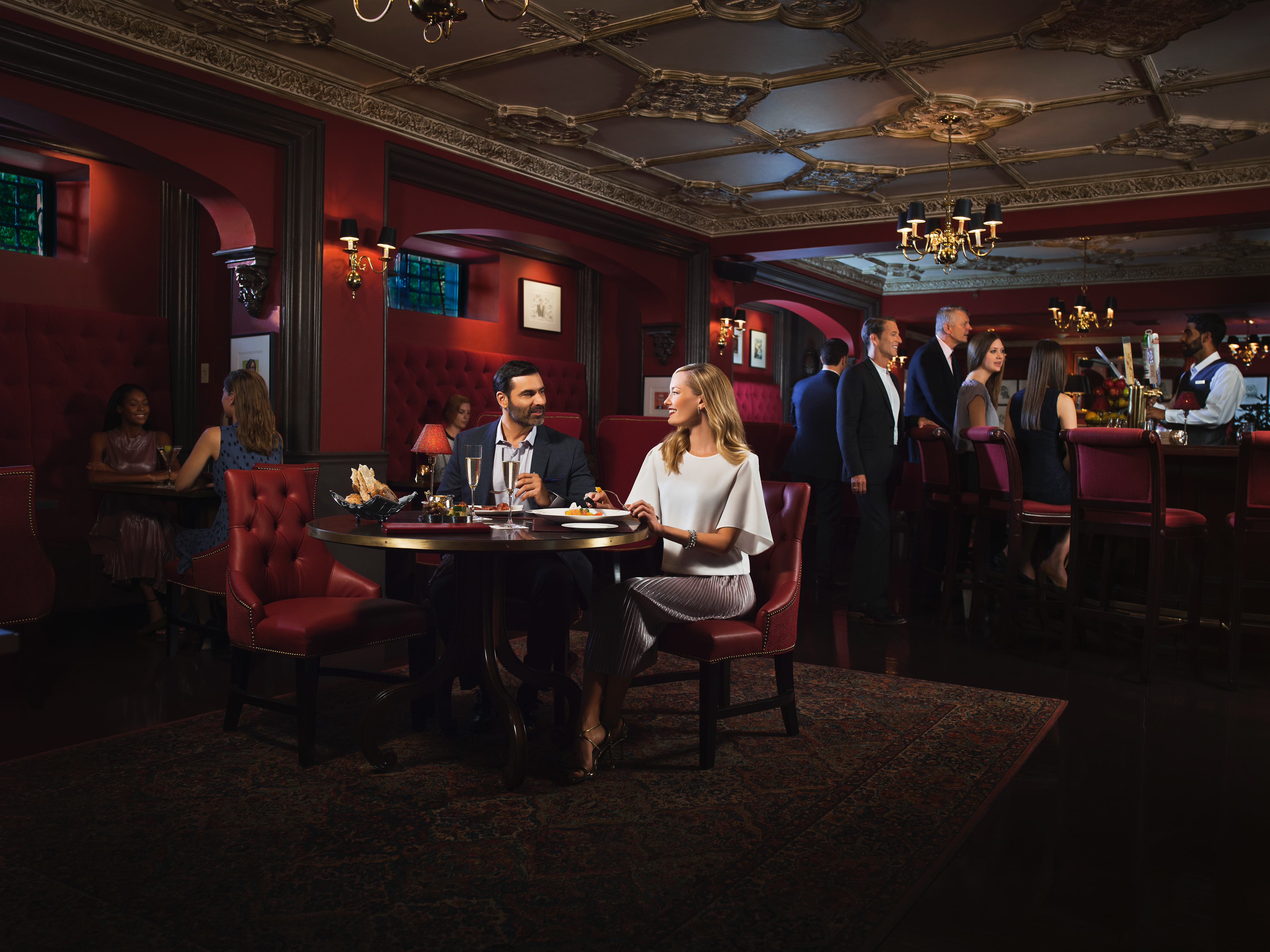 A couple dining at a table in a luxurious lounge with red walls and booth seating.